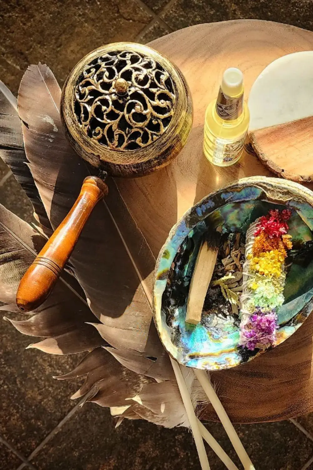 Ceremony objects on a wooden board: feathers, an abalone shell with dried petals, a brass incense holder, and a small bottle of oil.