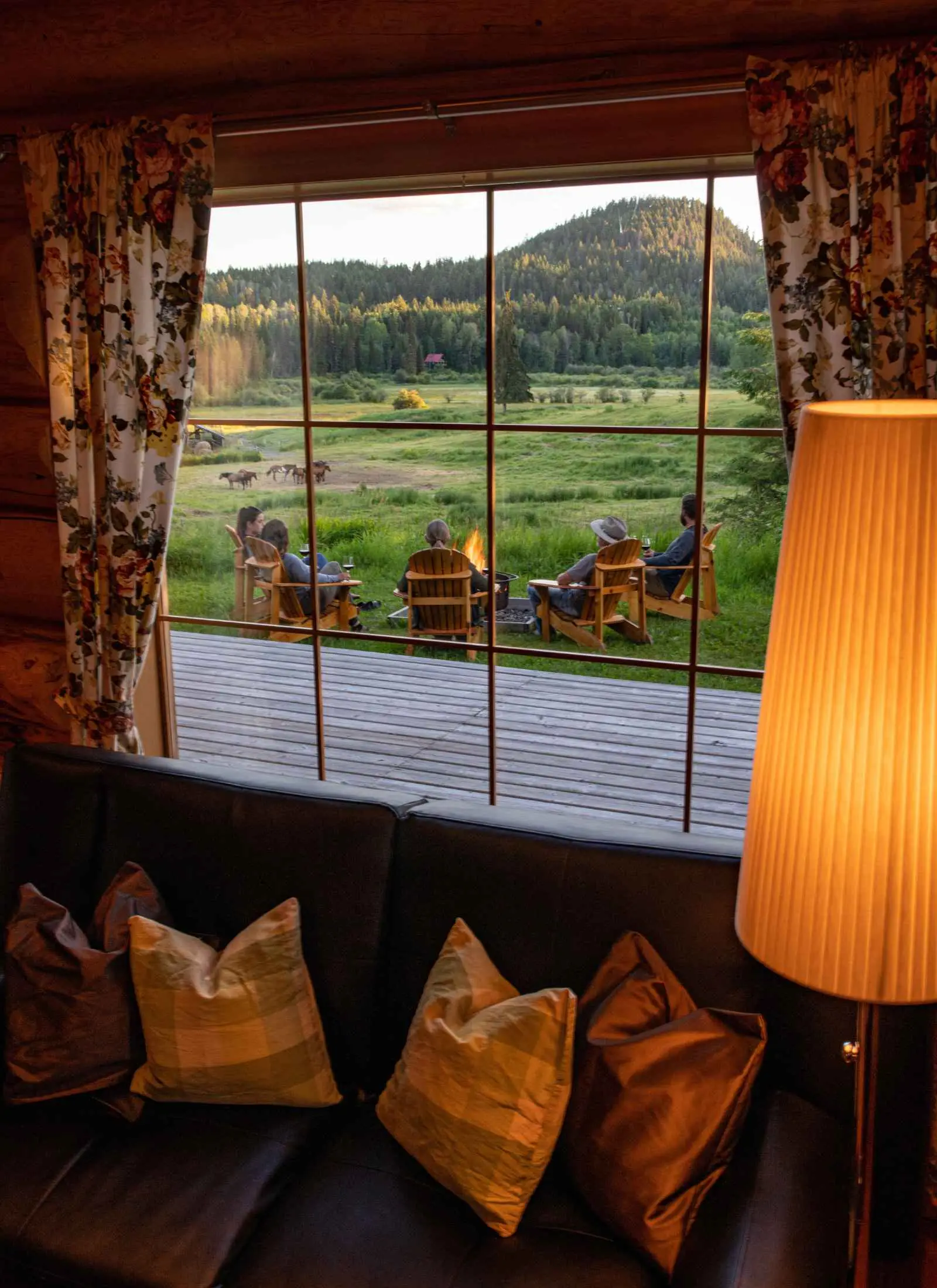 A cabin sitting room at Kayanara with cushions and a lit lamp, looking out to the deck and the fire.